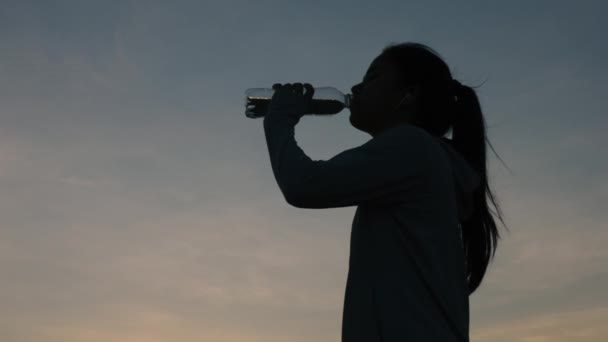 シルエットの若いアジアの女性は山の中で外の夕日をワークアウトした後 飲料水を実行しています 健康的なスポーツランニングのコンセプト — ストック動画