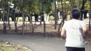 Yakışıklı, Asyalı bir adam parkta koşuyor. Orman konseptinde sporcu idmanı sağlıklı bir şekilde yapar..
