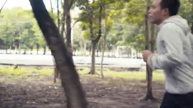 Genç Asyalı bir adam parkta koşuyor. Orman konseptinde sporcu idmanı sağlıklı bir şekilde yapar..