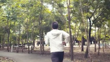 Genç Asyalı bir sporcu halka açık bir parkta koşuyor ve güzel ormanların tadını çıkarıyor. Kamu parkı konseptinde sporcu eğitimi..