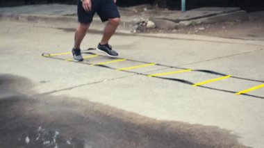 Asyalı koşucular çeviklik merdiveni ekipmanlarıyla eğitim görüyorlar. Kamu parkı konseptinde sporcu eğitimi..