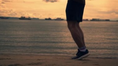 Yazın güzel bir gün batımında sahilde egzersiz yaparken ip atlayan Asyalı sporcu bacaklarını kapat. Sağlıklı spor yaşam tarzı konsepti.