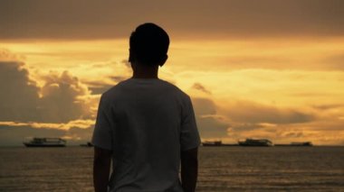 Kulaklık takan yakışıklı bir sporcunun silueti sahilde dururken müzik dinliyor ve yazın güzel gün batımını seyrediyor..