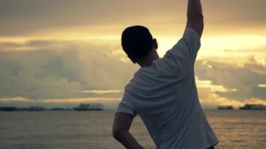 Asyalı koşucunun silueti sahilde koşmadan önce gerinirken yazın güzel bir gün batımı. Açık hava idman konsepti.