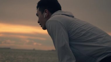 Yorgun Asyalı sporcu yaz aylarında güzel bir günbatımında sahilde koşan antrenmandan sonra nefes alıyor. Sağlıklı spor yaşam tarzı konsepti.