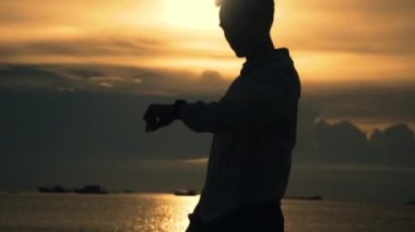 Sporcunun silueti kardiyo egzersizi yapıyor. Sahilde dururken kalp atışlarını kontrol ediyor. Yazın gün batımı çok güzel..