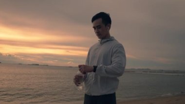 Asyalı sporcu sahilde güzel gün batımında su içerken. Sporcu eğitim egzersizi sağlık konsepti.