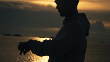 Sporcunun silueti kardiyo egzersizi yapıyor. Sahilde dururken kalp atışlarını kontrol ediyor. Yazın gün batımı çok güzel..