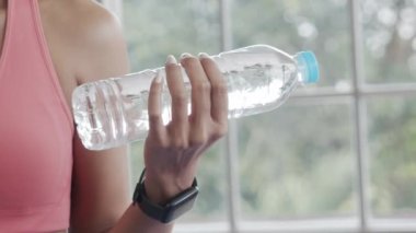 Spor kıyafetli, yakın plan Asyalı kadın elinde su şişesi ağırlığı yogası egzersizi ile evdeki oturma odasında..