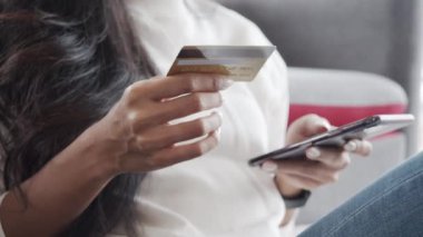 Kapatın ellerinizi, kredi kartı ve akıllı telefon taşıyan Asyalı genç bayan müşteri evdeki kanepede oturuyor. Yaygın COVID-19 sırasında seyyar alışveriş yapan kadınlar çevrimiçi mağazalar kullanıyor.