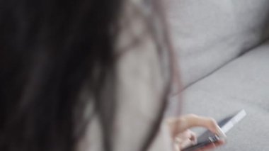 Paketi kontrol eden genç bir Asyalı kadın, karantina sırasında evdeki oturma odasındaki kanepede otururken akıllı telefon uygulamasında sipariş veriyor..