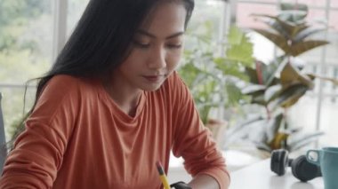 Asyalı yaratıcı kadın, evden çalışırken not defterine büyük projeler yazıyor.. 