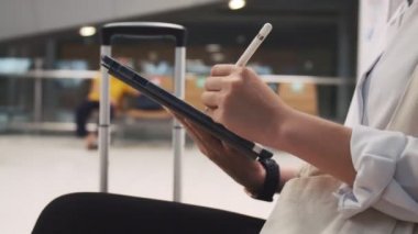 Kadın tabletini çizerken ellerinizi kapatın ve havaalanı terminalinde bir sandalye otururken tableti kontrol edin ve COVID-19 salgını sırasında sosyal mesafeyi koruyun..