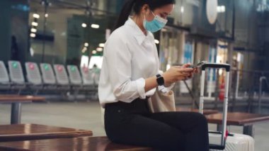 Cerrahi maske takan iş kadını havaalanı terminalindeyken arkadaşlarıyla telefonda konuşuyor ve COVID-19 salgını sırasında sosyal mesafeyi koruyor..