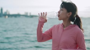 Dişi koşucu sahilde dikilirken su içiyor. Eğitimden dinlenirken su şişesinden içen aktif bir kadın..