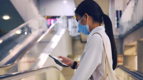 在机场候机楼的自动扶梯上 佩戴口罩和使用智能手机的女商人在Covid 19大流行期间保持社交距离 — 图库视频影像