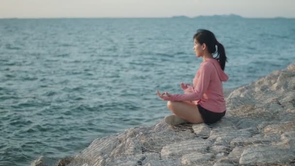 Asiatisk Atletisk Kvinna Mediterar Sitter Stenar Havet Medan Solnedgången Zen — Stockvideo