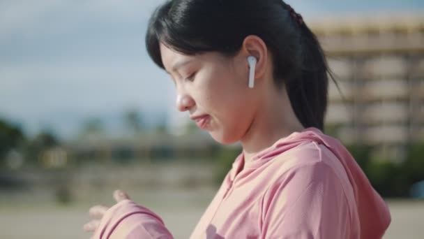 운동을 하다가 휴식을 취하고 아시아 소녀가 아름다운 해변에서 마시고 활동적 — 비디오