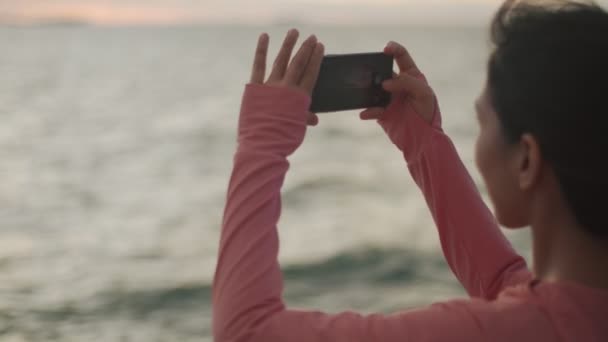 在美丽的夕阳西下站在海滩上做完运动后 用智能手机拍摄了一张大海的照片 — 图库视频影像