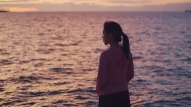 Genç Asyalı bir kadının portresi. Huzurlu günbatımının keyfini çıkarıyor ve güzel okyanus manzarasını rahatlatan temiz hava soluyor..