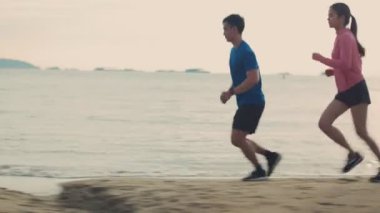 Sahilde koşan Asyalı çift spor koşucusu. Güzel bir gün batımında koşuya çıkan kadınlar, koşucuları geçiyor. Sağlıklı yaşam tarzı kavramı.