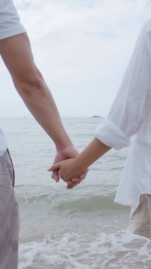 Dikey Video: Çekici Asyalı çift sahilde romantik günbatımını seyrediyor ve deniz manzaralı günbatımını seyrediyor, tatilde Tayland 'da güzel okyanusa seyahat eden çift hafta sonu.