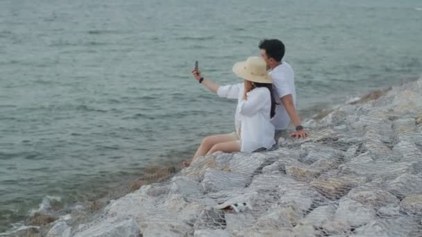 Szczęśliwa Azjatycka Para Korzystająca Smartfona Robi Zdjęcie Selfie Siedząc Kamieniu — Wideo stockowe
