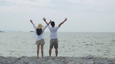 Aşık Asyalı çift hafta sonu tatilinde kollarını havaya kaldırarak başarıyı kutluyor. Plaj gezisinde romantik bir çift..