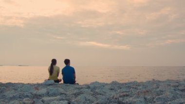 Genç çift koşuyor, koşuyor ve deniz kenarında oturup güzel gün batımını seyrediyor. Sağlıklı yaşam tarzı kavramı.