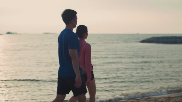 海辺でスポーツの練習をした後 ビーチを歩く若いカップルランナー 男と女の子のスポーティワークアウトライフスタイル屋外コンセプト — ストック動画