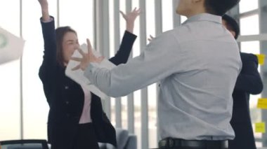 Bir grup Asyalı iş adamı dans ediyor ve modern ofisteki iş yerlerinde başarı kutlamaları yapıyor. Birlikte eğlenen bir iş, hedeflere ulaşmanın tadını çıkarıyor..