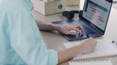 Covid-19 salgını sırasında ana ofiste Asyalı küçük işletme sahibi dizüstü bilgisayarla istatistik grafiği en çok satan ürünü kontrol ediyor..