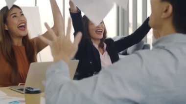 Asyalı iş adamlarından oluşan bir grup modern ofisteki iş yerlerinde başarıyı kutlayan belgeler atıyor. Birlikte eğlenen bir iş, hedeflere ulaşmanın keyfini çıkarıyor..