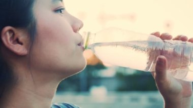 Antrenman sırasında su içen güzel bir Asyalı genç kadın, koşu, koşu, parkta yoga, egzersizden sonra kadın içme suyu..
