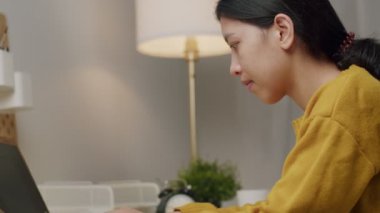 Güzel Asyalı kadın evde dizüstü bilgisayar kullanıyor ve internetten evdeki bilgisayarda araştırma yapıyor..