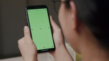 Kafkas bir kadının elinde krom anahtar, yeşil ekran akıllı telefonuyla çevrimiçi içeriği izlerken görüntüsü. Cep telefonu kullanan bir kadın, internette gezinen, evde içeriği izleyen.