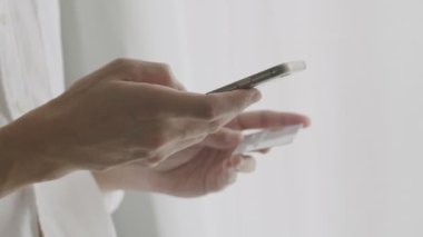 Yakın plan genç adam kredi kartı tutuyor ve COVID-19 salgını sırasında karantinaya alınırken akıllı telefon alışverişi yapıyor. İnternetten alışveriş kavramı.