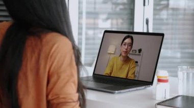 Asyalı iş kadını COVID-19 salgını sırasında evdeki bir video konferansında iş arkadaşlarıyla konuşuyor. Kendini izole etme, sosyal mesafeler, evde karantina. Evde çalışmak akıllıca..