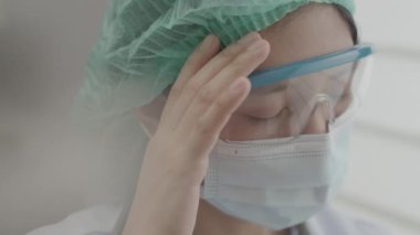 Doktor ya da hemşire baş ağrısından bitkin düşmüş ve koronavirüs salgını sırasında hastanede çalışırken şakaklarını ovuyor..