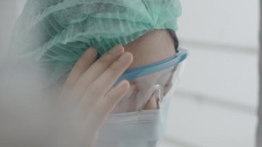 Yakın plan doktor ya da hemşire baş ağrısından bitkin düşmüş ve koronavirüs salgını sırasında hastanede çalışırken şakaklarını ovuyor. Sağlık çalışanları koruma altında..