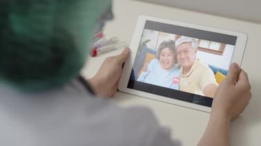 Kadın doktor COVID-19 salgını sırasında hastanede çalışırken anne ve babaya tablet video kullanıyor..