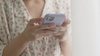 İnternetten akıllı telefon alışverişi yapan Asyalı kadını kapatın, evdeki oturma odasının penceresinin yanında dururken sosyal medya haberleri seyredin..