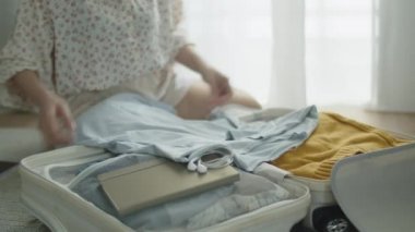 Çekici bir Asyalı kadın valizini topluyor ve giysi, alet edevat, kitap, kulaklık takıyor yaz tatiline gitmek için hazırlanıyor..