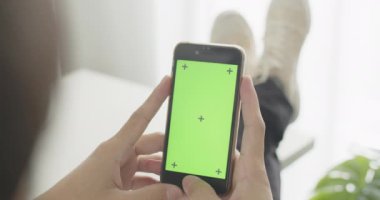 Asyalı bir adam ofis odasında krom tuşlu yeşil ekranlı akıllı telefon kullanıyor, sosyal medyada geziniyor ya da online içeriği, iletişim konseptini izliyor..
