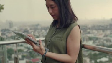 Kadınlar arkadaşlarıyla sohbet etmek için tabletleri kullanır. Gün batımında binanın çatısındaki bir balkonun yanında dikilirken..