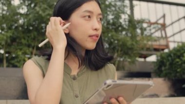 Gün batımında çatıda otururken tablet kullanan Asyalı kadın..