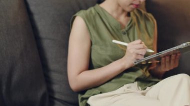 Asyalı kadın, gece vakti oturma odasındaki kanepede otururken dijital tabletinden haber okuyor..