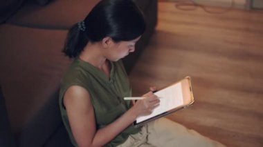 Asyalı kadın, gece vakti oturma odasındaki kanepede otururken dijital tabletinden haber okuyor..