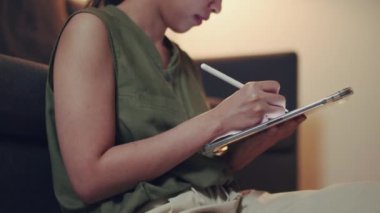 Asyalı kadın, gece vakti oturma odasındaki kanepede otururken dijital tabletinden haber okuyor..