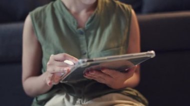 Yakın çekim el, oturma odasındaki kanepede otururken dijital tabletine yazı yazmak için kalem kullanıyor..